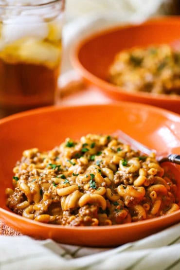 A close-up view of an orange dinner bowl filled with a serving of homemade cheesy hamburger helper.
