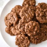 A close-up view of a pile of double chocolate chip cookies sitting on a white plate.