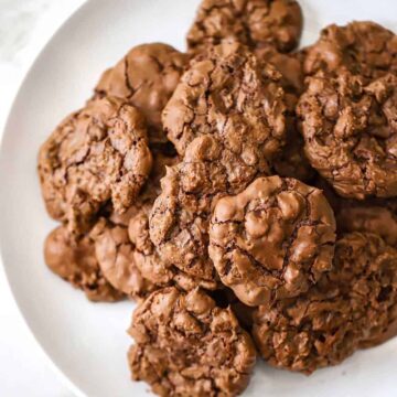 A close-up view of a pile of double chocolate chip cookies sitting on a white plate.