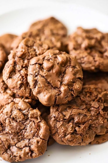A close-up view of a pile of double chocolate chip cookies sitting on a white plate.