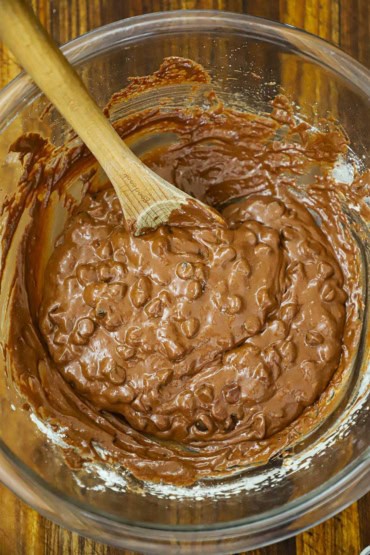 An overhead view of a large glass bowl filled with double chocolate chip cookie batter with a wooden spoon inserted in the side.