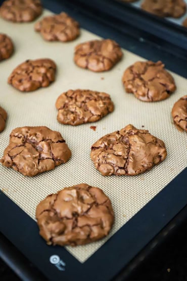 A straight-on view of a cookie sheet that is lined with a silicone baking mat and is topped with freshly baked double chocolate chip cookies.
