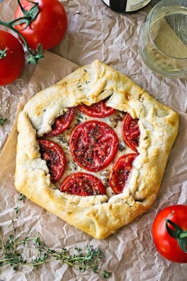 An overhead view of a baked galette that is filled with roasted sliced tomatoes sitting on top of melted cheese and is sitting on crumpled butcher paper.