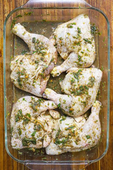 An overhead view of uncooked whole chicken legs that are covered in jerk marinade in a large glass baking dish.