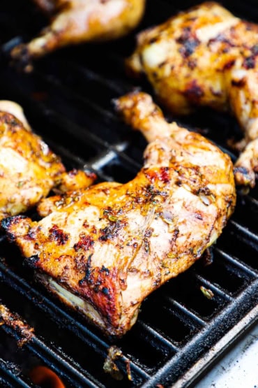 A close-up view of whole chicken legs that are being grilled and lightly charred on a gas grill.