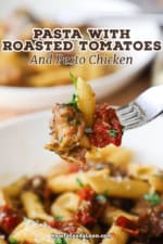 A close-up view of a person holding a fork up that has a roasted tomato, cooked penne pasta, and grilled pesto chicken on it.