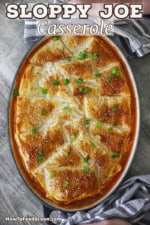 An overhead view of sloppy Joe casserole in an oval baking dish that is topped with browned puff pastry and garnished with sesame seeds and chopped scallions.