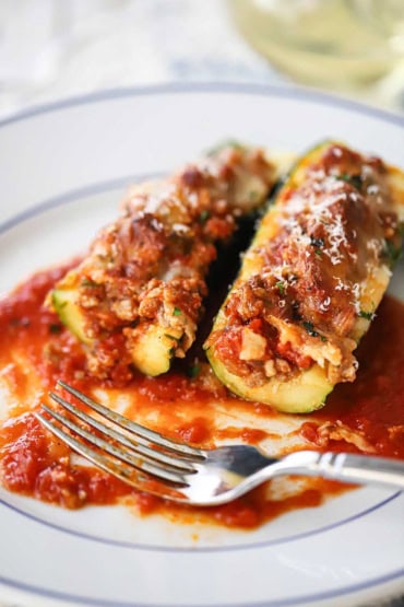 A close-up view of two stuffed zucchini boats that are resting on a bed of marinara sauce and have both been partially eaten.