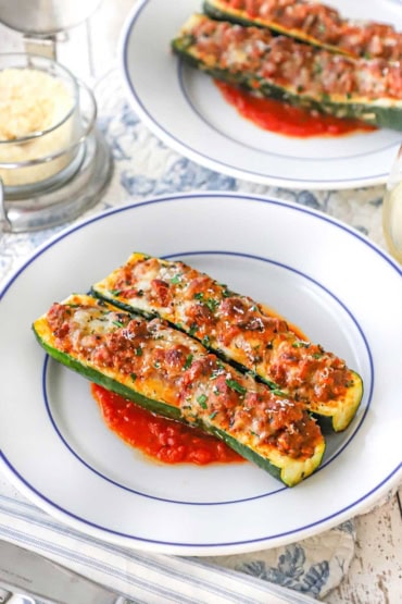 A straight-on view of two white dinner plates filled with two stuffed zucchini boats that are resting on a small layer of marinara sauce.