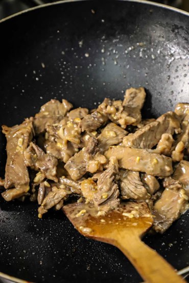 A close-up view of strips of beef ribeye that are being stir-fried in a non-stick wok in a soy and ginger sauce.