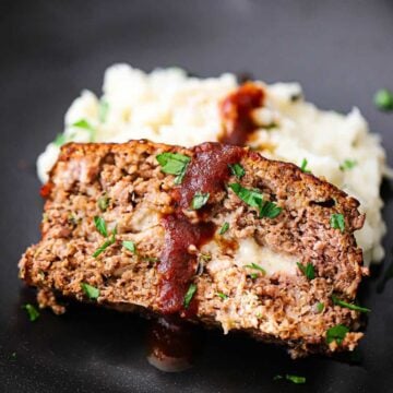 A close-up view of a slice of cheese-stuffed smoked meatloaf resting on a pile of mashed potatoes on a black plate.