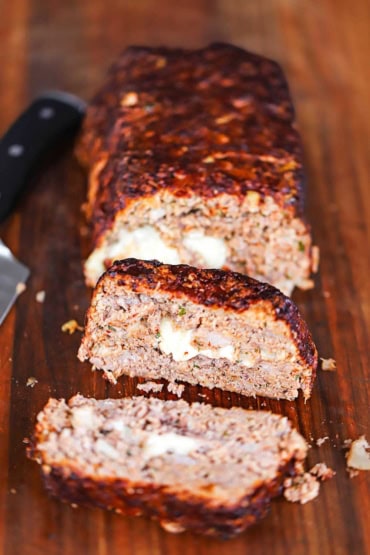 A straight-on view of a cheese-stuffed smoked meatloaf with several slices visible on a large wooden cutting board.