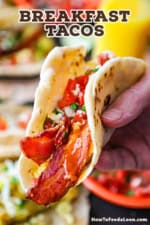 A person holding up a breakfast taco that is made with a homemade flour tortilla and is stuffed with eggs, bacon, cheese, and topped with pico de gallo.