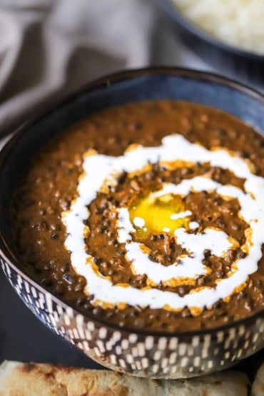 A close-up view of a colorful bowl that is filled with a serving of dal makhani that is topped with a circular formation of cream and a pat of melting butter in the center.