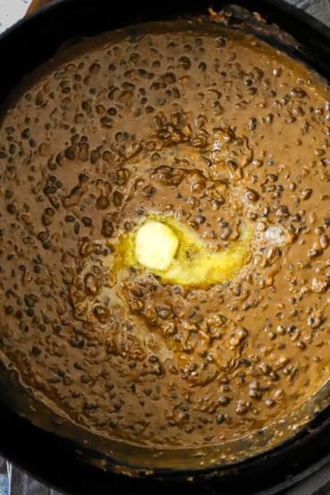 An overhead view of a large pot of dal makhani with a pat of butter that is melting in the center of it.