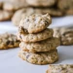 A straight-on view of four homemade oatmeal cookies stacked on top of each other on a piece of parchment paper with other similar cookies nearby.
