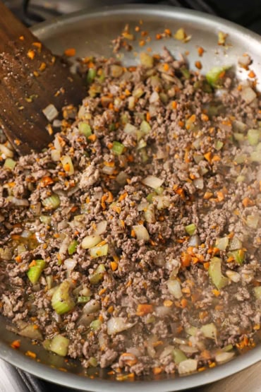 A straight-on view of a cooked ground beef mixture combined with sautéed onions, carrots, celery, and simmered with red wine.
