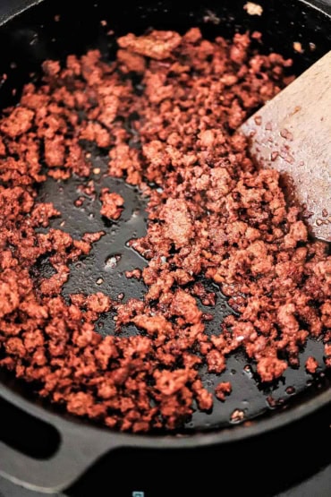 A view looking into a large cast-iron skillet that is filled with fully cooked chorizo sauce with a wooden spatula off to the side.