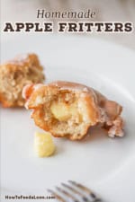 A close-up view of an apple fritter that has been broken in half so the interior is visible including small chunks of cubed apples.