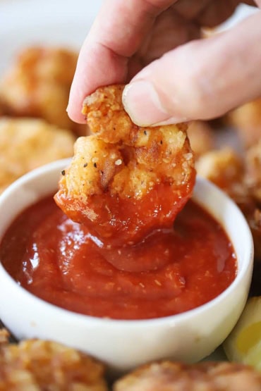 A close-up view of a person plunging a Southern fried shrimp into a bowl of homemade cocktail sauce.