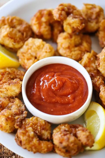 A straight-on view of a platter of Southern fried shrimp with a small bowl of homemade cocktail sauce in the middle.