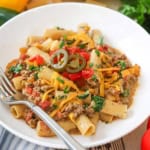 A straight-on view of a white bowl filled with a serving of Tex-Mex pasta topped with chopped cilantro, tomatoes, and a couple of pickled jalapeño slices.
