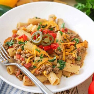 A straight-on view of a white bowl filled with a serving of Tex-Mex pasta topped with chopped cilantro, tomatoes, and a couple of pickled jalapeño slices.