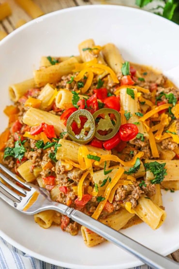 A straight-on view of a white bowl filled with a serving of Tex-Mex pasta topped with chopped cilantro, tomatoes, and a couple of pickled jalapeño slices.