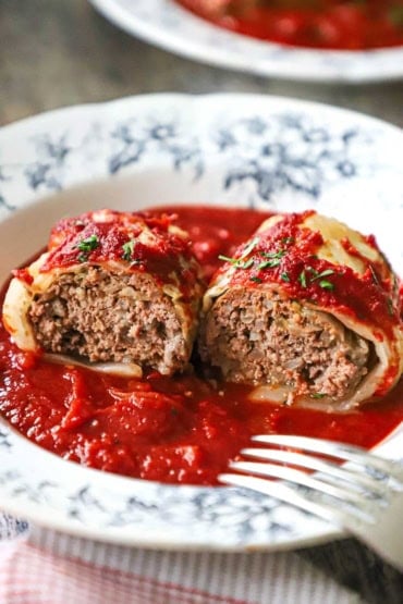 A straight-on view of a stuffed cabbage roll with tomatoes sauce that has been split in half and spread open so the beef and rice filling is visible.