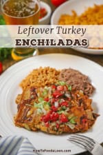 A straight-on view of a white dinner plate filled with two leftover turkey enchiladas next to a serving of refried beans and Mexican rice with a glass of beer in the background.