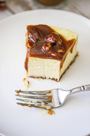 A straight-on view of a half eaten slice of pecan pie cheesecake on a white dessert plate with a fork also resting on the plate.