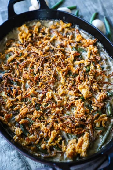A straight-on view of a large oval baking dish that is filled with gourmet green bean casserole and topped with fried onion strips.