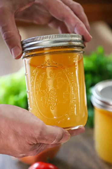 A person using two hands to hold a glass Mason jar filled with homemade vegetable stock.