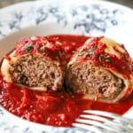A straight-on view of a stuffed cabbage roll with tomatoes sauce that has been split in half and spread open so the beef and rice filling is visible.