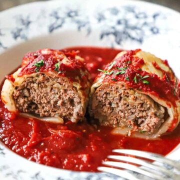 A straight-on view of a stuffed cabbage roll with tomatoes sauce that has been split in half and spread open so the beef and rice filling is visible.
