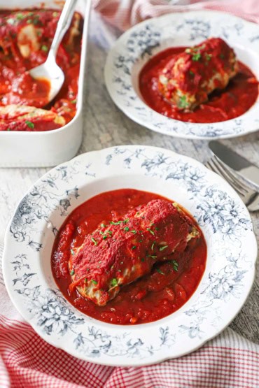Two vintage serving bowl filled with single servings of stuffed cabbage rolls ina rich tomato sauce.