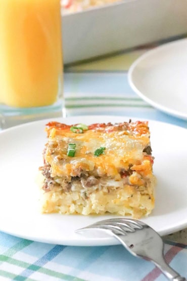 A straight-on view of square piece of a breakfast casserole with a top layer of melty cheese over sausage sitting on a bed of shredded potatoes.