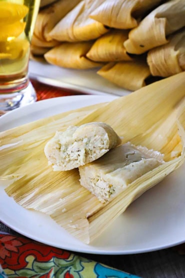 A close-up view of a homemade tamale that has been cut in half so the chicken and chilis filling is revealed.