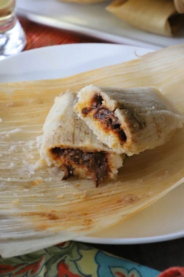 A close-up view of a pork tamale that has been cut in half and one end is resting on the other end so filling is visible.