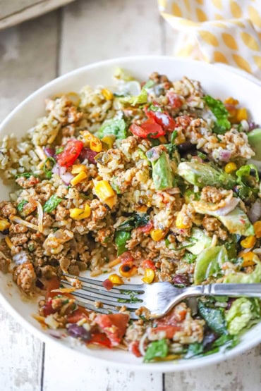 A close-up view of a white bowl filled with a turkey burrito bowl that has been stirred together and partially eaten with a fork inserted into the side.
