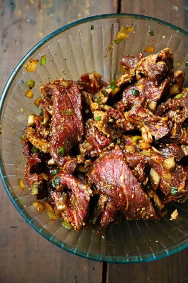 An overhead view of a glass bowl that is filled with thin strips of ribeye steak that has been coated in a Korean marinade.