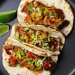 An overhead view of three Korean beef tacos with kimchi pressed against each other and topped with Korean bbq sauce and slivers of green onions.