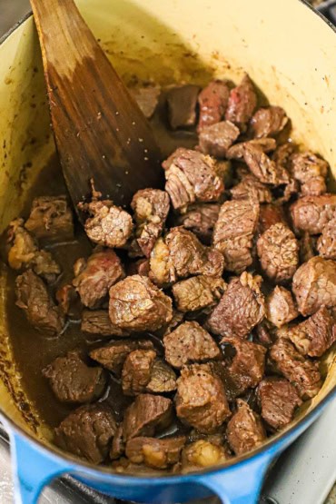 An overhead view of a large oval Dutch oven that is filled with bite-sized chunks of seasoned stew meat that have been seared.