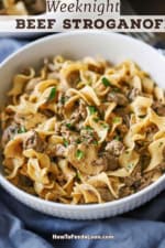 A close-up view of a white shallow bowl filled with a serving of weeknight beef stroganoff with a light blue napkin wrapped around the bottom of the bowl.