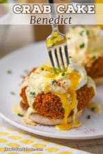 A close-up view of a fork being used to break open a poached egg that is resting on top of a crab cake that is on the bottom of a toasted English muffin.
