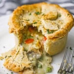 A close-up view of a homemade chicken pot pie with an upper crust and a lower crust that has been broken open with the innards pouring out onto the plate.