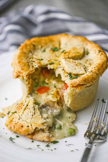 A straight-on view of a homemade chicken pot pie with a top and bottom crust that has been cut open with the creamy chicken innards pouring out onto the plate