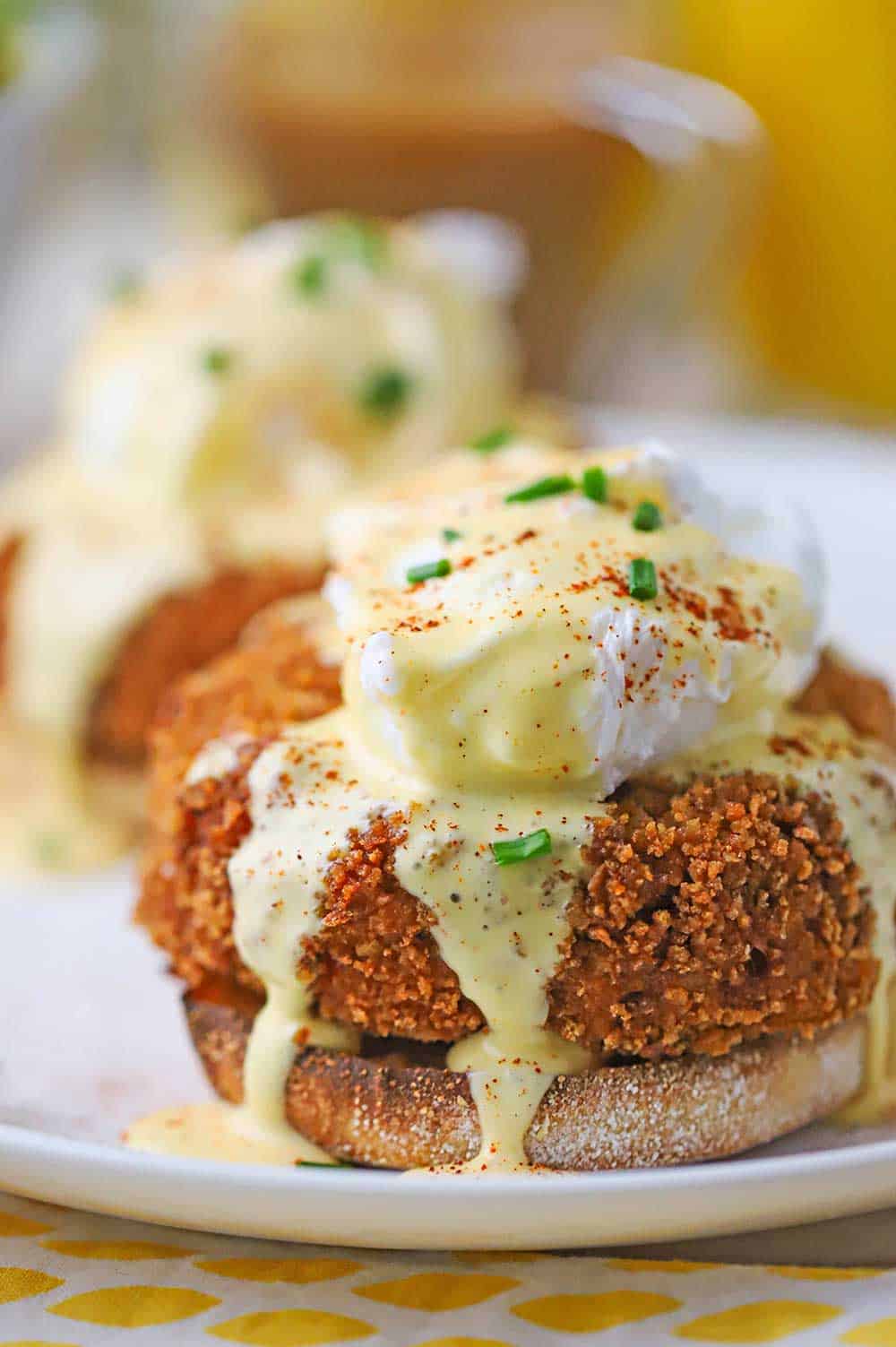 A close-up view of an untouched crab cakes egg Benedict with hollandaise flowing over the top of the poached egg and pooling on a white plate.
