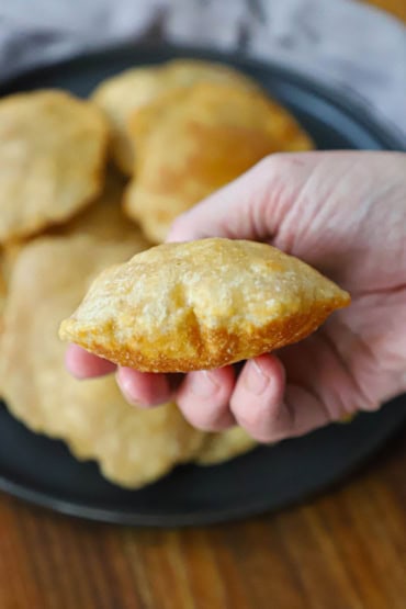 A close-up view of a person holding a puffy Indian fried bread poori in his hand over a black circular platter holding more poori.