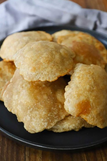 A close-up view of a pile of puffy fried Indian bread called poori and they are sitting on top of each other on a black plate.